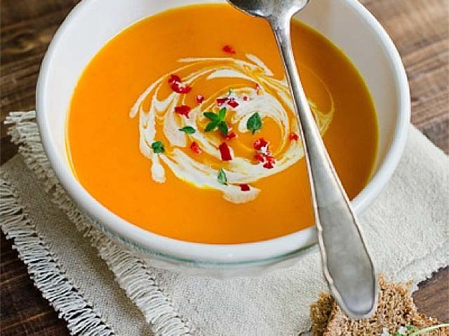 Bowl of pumpkin soup on place mat with bread