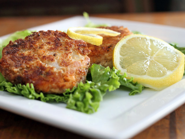 salmon cakes on a white plate with green lettuce and lemon slices