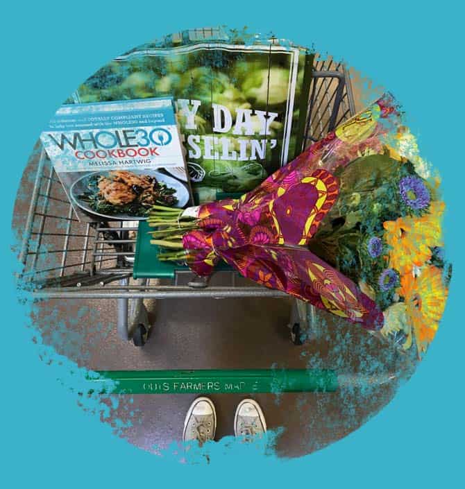 A shopping cart with Whole30 meal plan cookbook and fresh flowers.