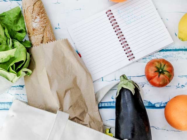 Meal planning notebook with fresh vegetables, loaf of bread against white and teal wood