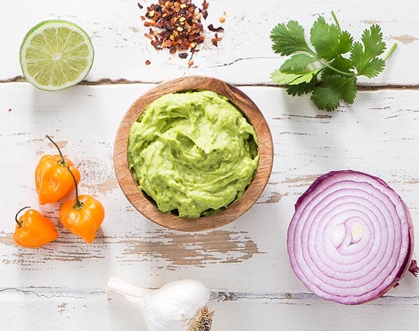 Fiery guacamole in a bowl surrounded by ingredients