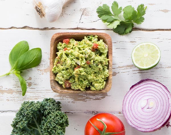 Garden guacamole in a bowl surrounded by ingredients