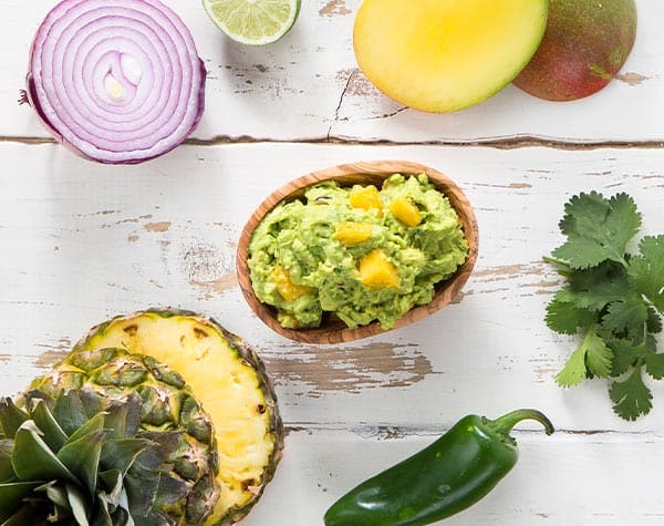 Tropical guacamole in a bowl surrounded by ingredients