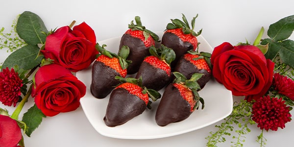 Chocoloate dipped strawberries surrounded by roses