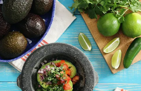 Bowl of avocados next to bowl of guacamole surrounded by limes.